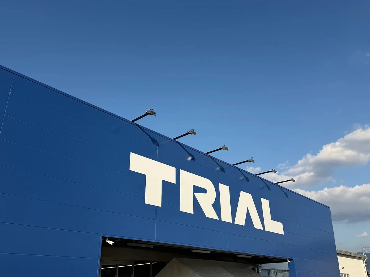 青い外壁に白いTRIALのロゴが入ったトライアル店舗の看板と青空(イメージ)