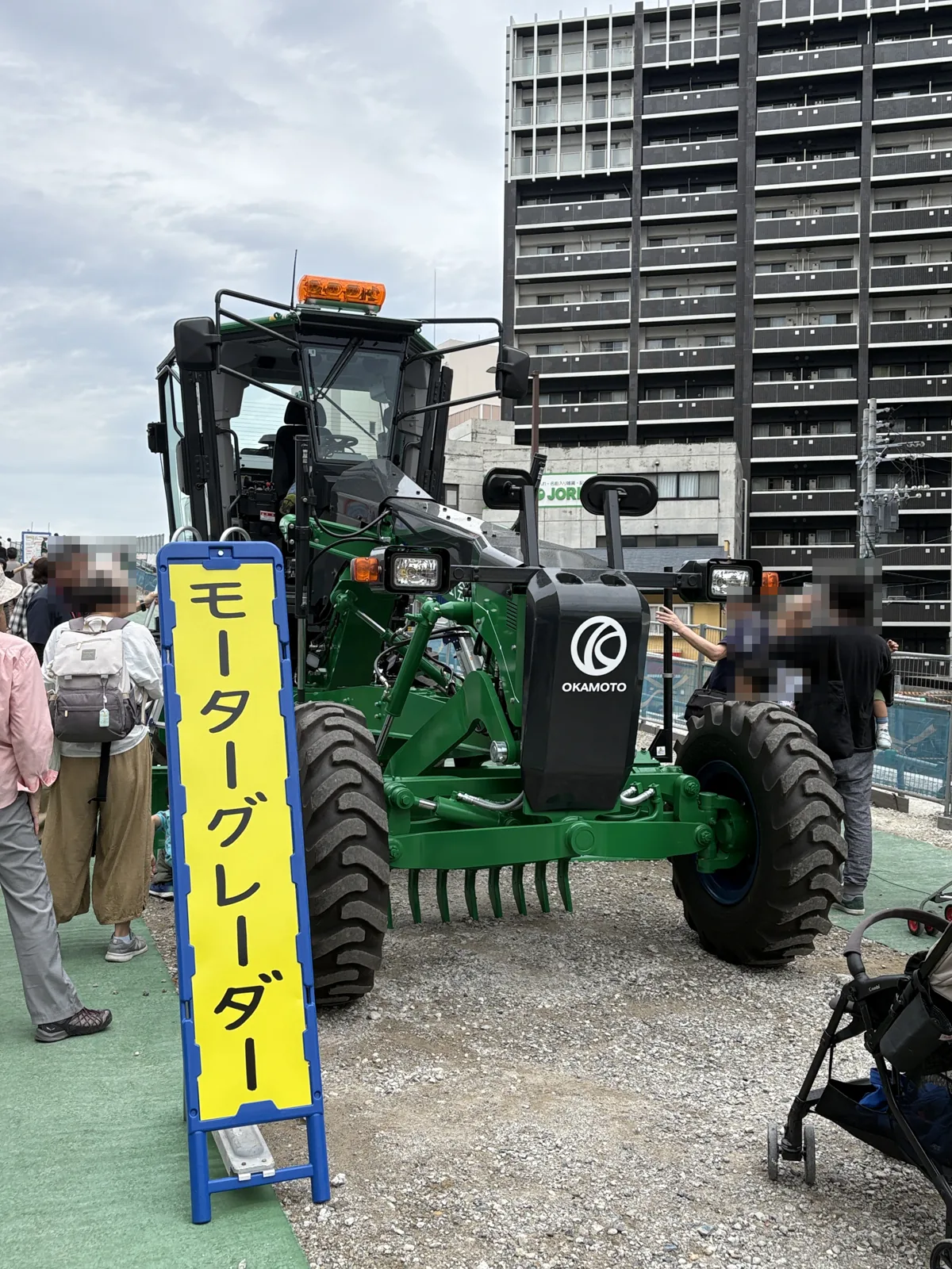 「モーターグレーダー」の看板と、緑色のモーターグレーダー
