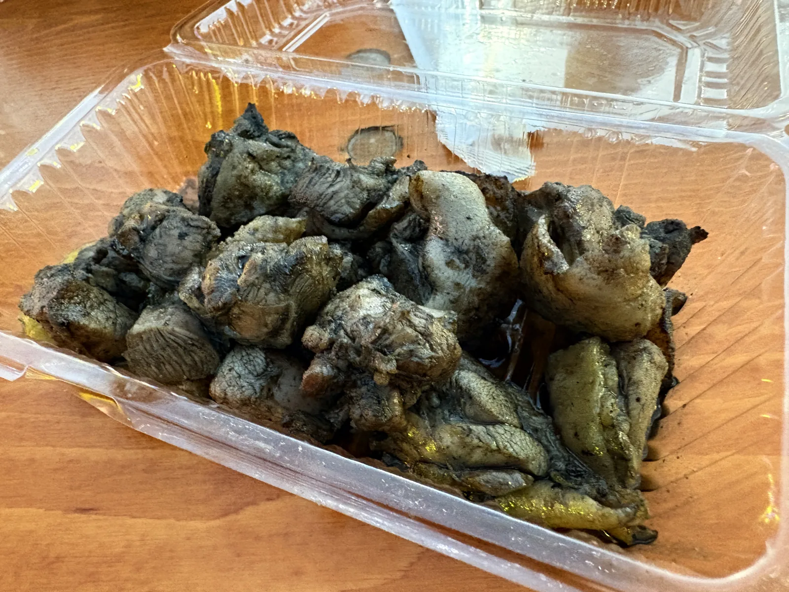 炭火家の地鶏の炭火焼き。炭で黒く焼き色のついた地鶏がパックに盛られている