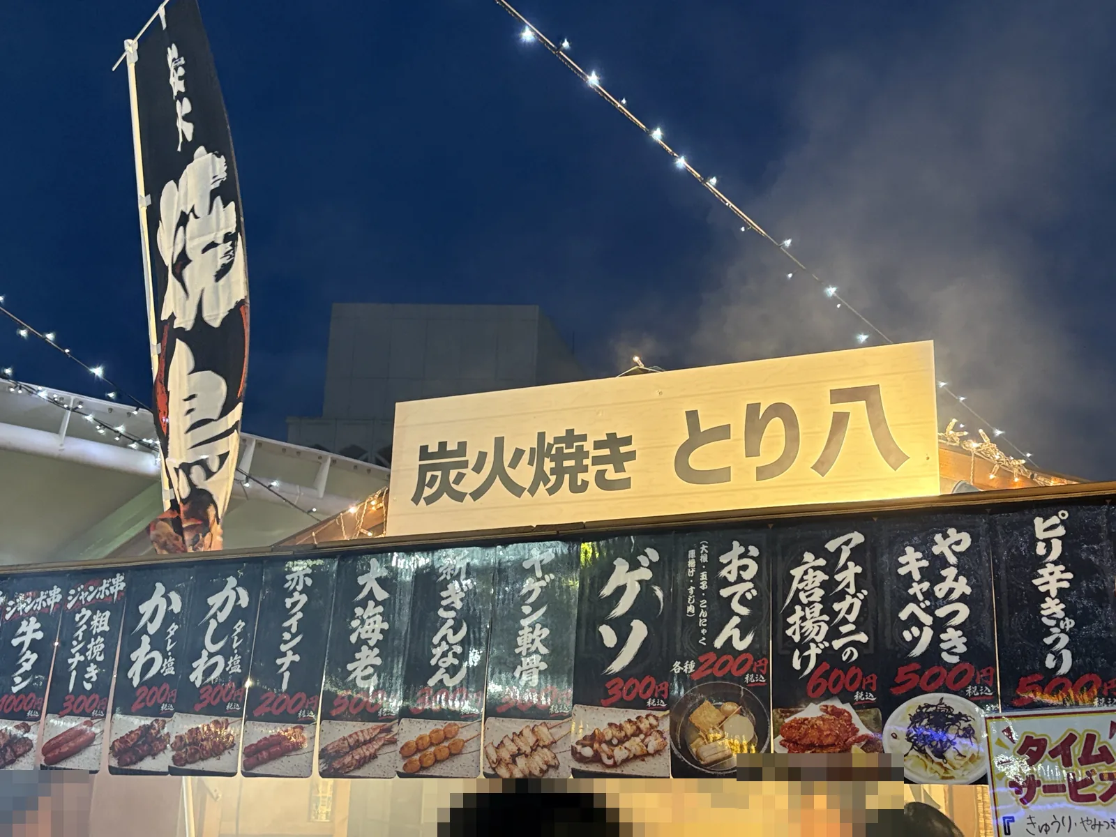 炭火焼き とり八の屋台。牛タンや大海老のジャンボ串、かわ、かしわ、おでんなどのメニューが並び、奥から煙が上がる