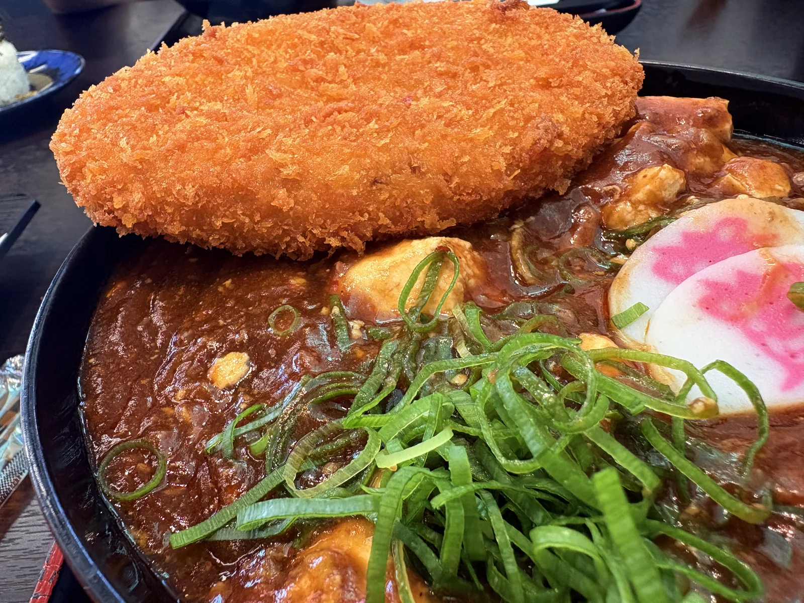麻婆丼にコロッケをのせたところ。大判のコロッケが丼の半分を覆う