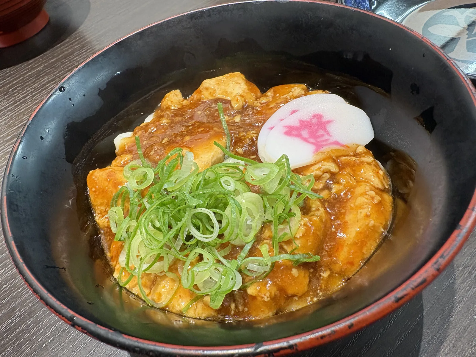 資フェスVol.2で出た試作の麻婆うどん。黒い丼に麻婆豆腐、刻みネギ、「資」のかまぼこ