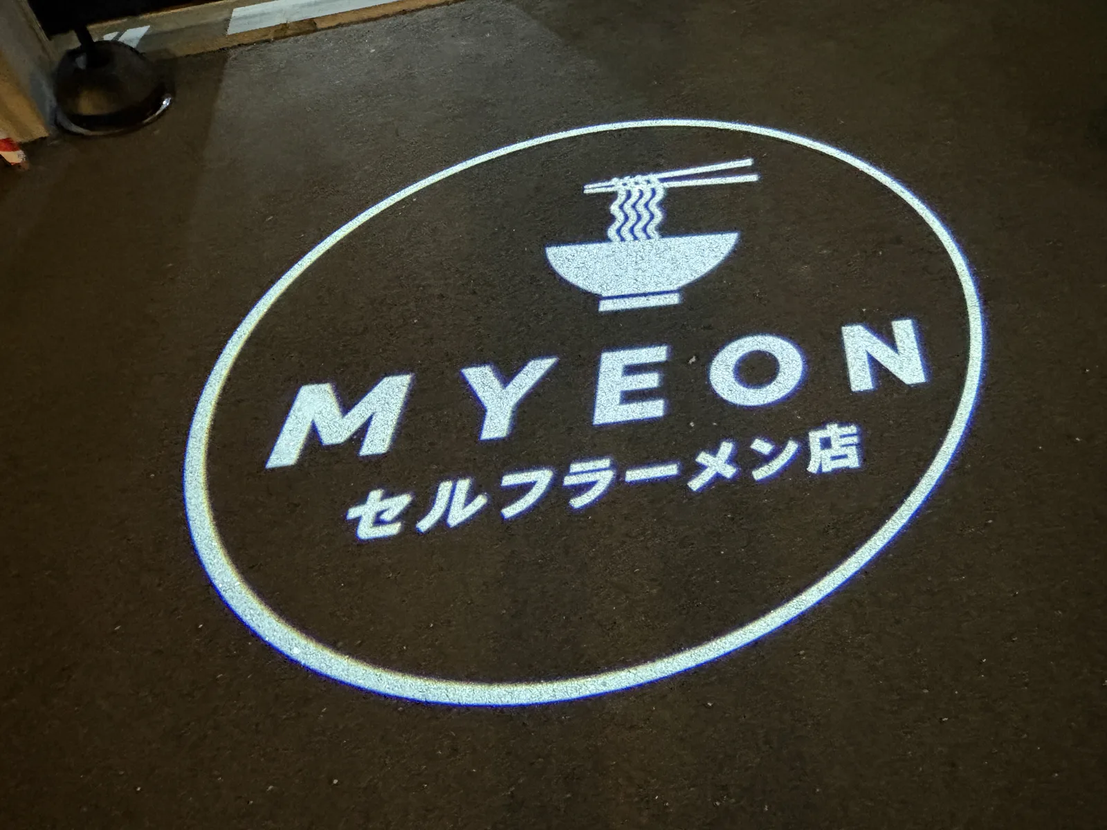店の前の路面に投影されたMYEONのロゴ。「MYEON セルフラーメン店」
