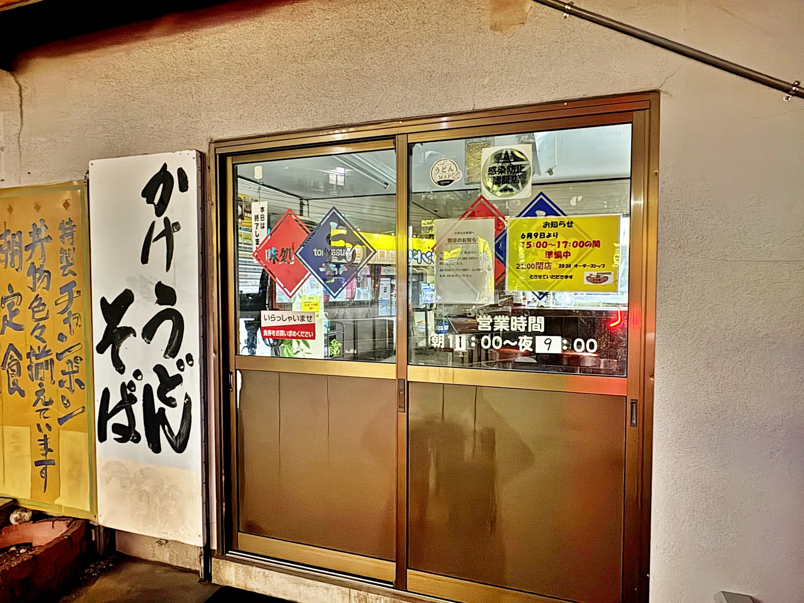 入口。「かけうどん そば」の看板と、ドアに「営業時間 朝11:00〜夜9:00」の表示