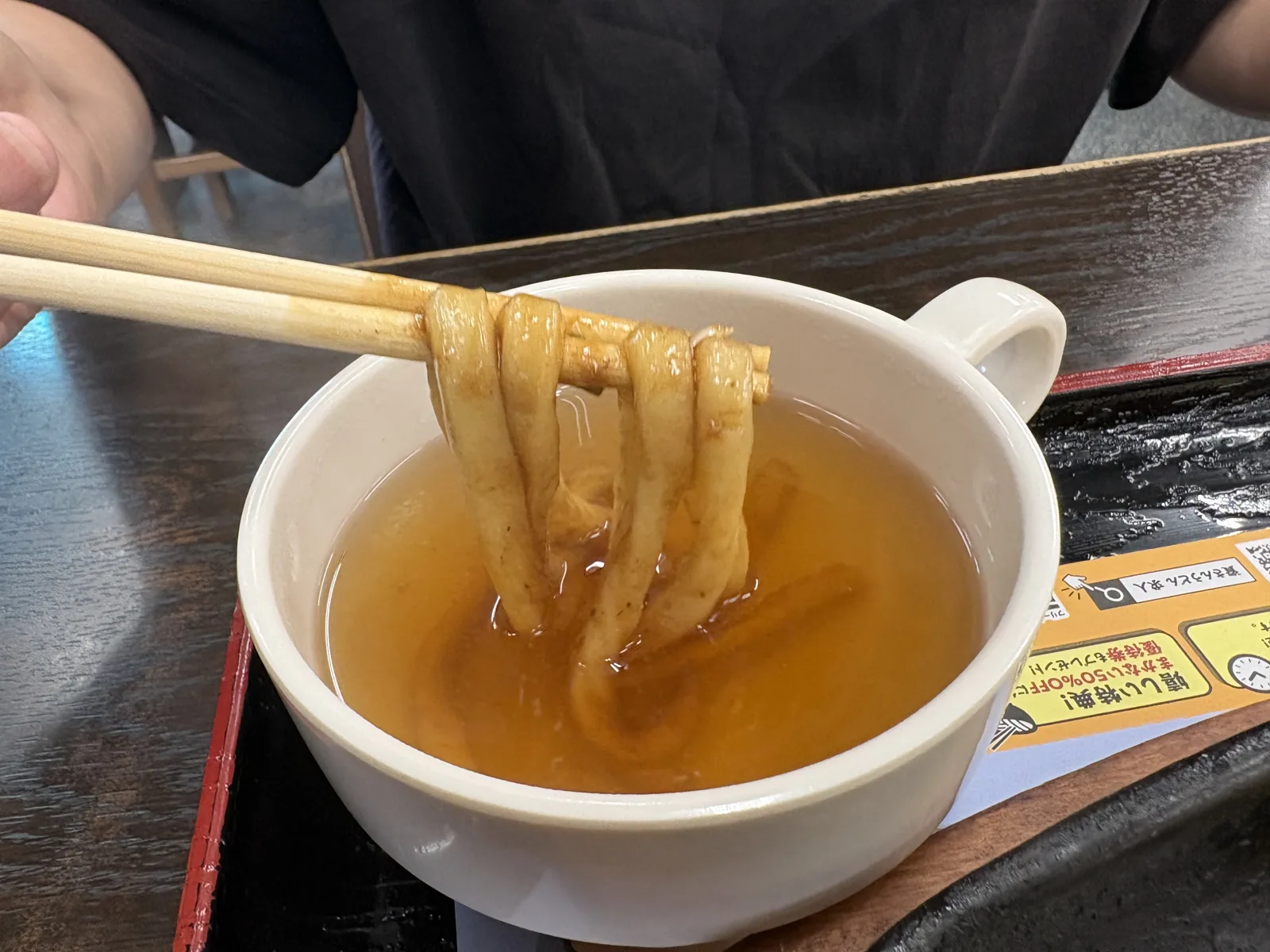 箸で持ち上げた焼きうどんを出汁のカップにくぐらせている